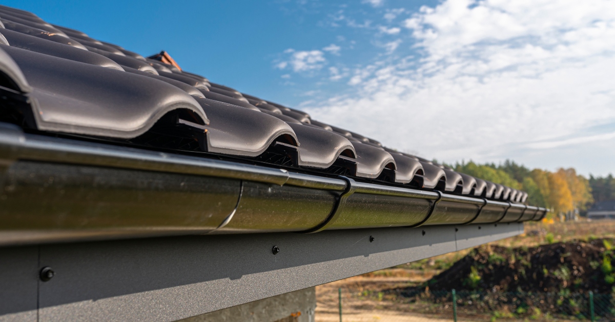 A metal, black gutter on a roof covered with ceramic tiles